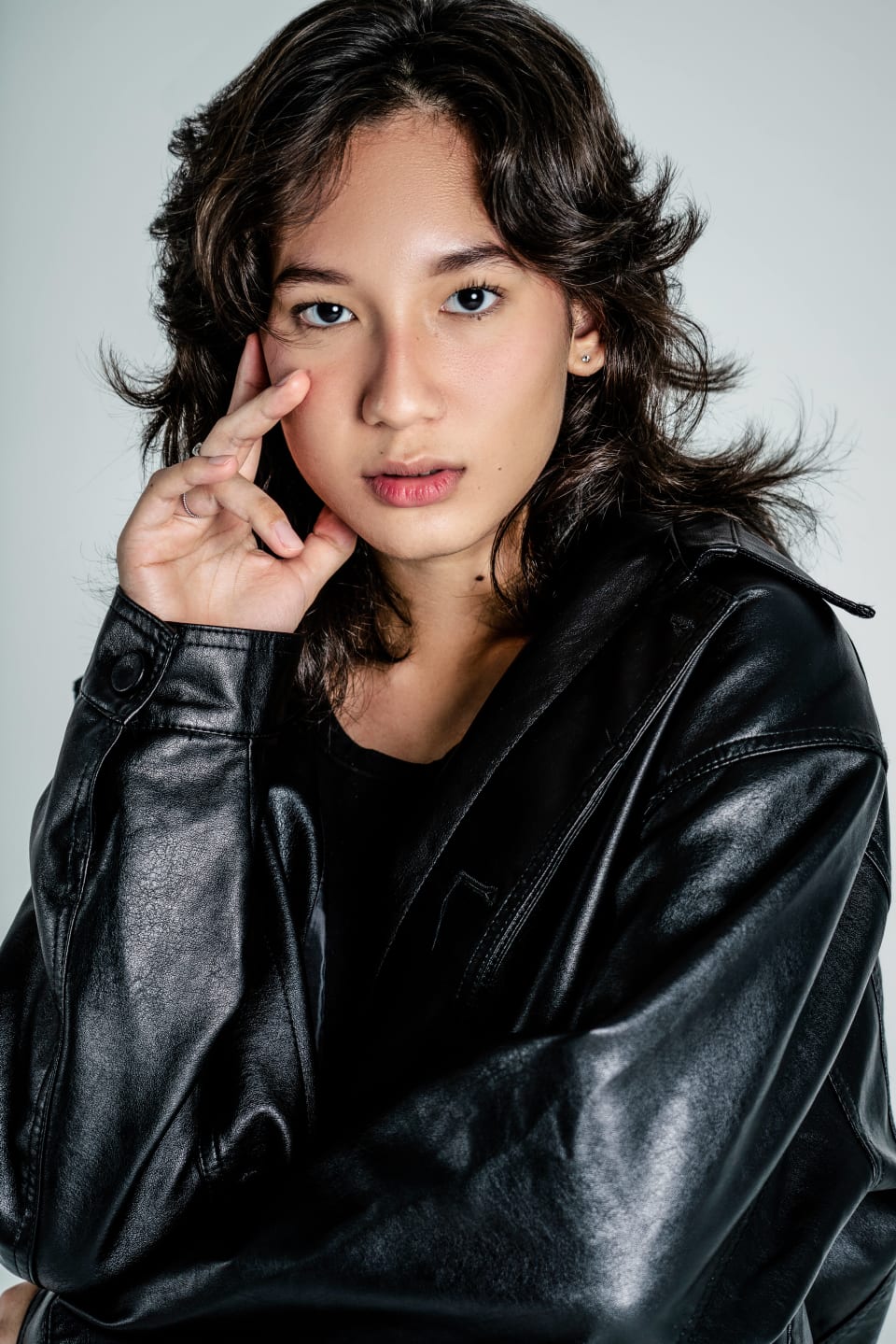 Close portrait, hand near face, leather jacket, direct gaze