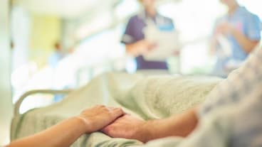 Une épidémie de grippe toujours intense et mortelle en janvier 2025. Une femme tient la main d'une personne âgée allongée sur un lit d'hôpital, avec des soignants à son chevet.