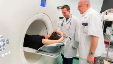 Pourquoi on fait un PET scan ? Deux soignants préparent une patiente à rentrer dans un PET scan.