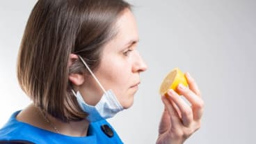 Anosmie : le trouble de l'odorat, ses causes et conséquences. Journée mondiale du 27 février 2025. Une femme ayant ôté son masque tente de sentir une moitié de citron.