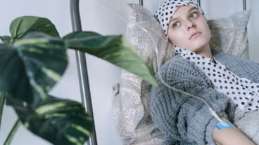 Cancer : semaine nationale de lutte 2025. Image d'une jeune femme sur un lit d'hôpital, le crâne protégé par un foulard.