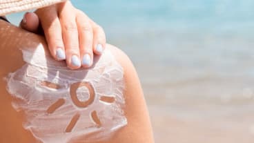 Peut-on attraper un cancer de la peau sans avoir eu de coup de soleil ? Image du dos nu d'une personne sur la plage, avec de la crème solaire sur laquelle on a dessiné un soleil.