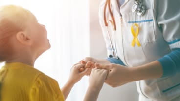 Septembre en or, mois contre le cancer des jeunes : une soignante tient les mains d'un enfant dans les siennes.