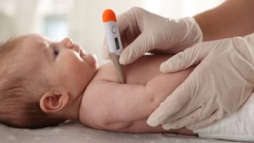 L’essentiel sur la bronchiolite, l’épidémie 2025 et les moyens de se protéger. Image d'un nourrisson allongé avec la main d'un soignant en train de prendre sa température sous le bras.