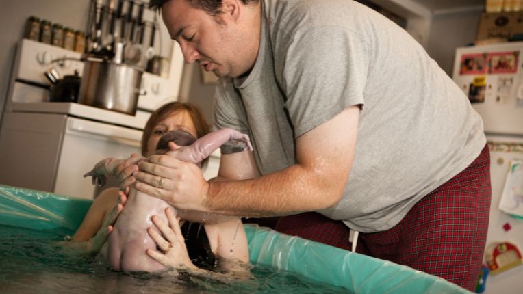 Accouchement dans l'eau - Photo d'une mère et son enfant dans une piscine, suite à un accouchement dans l'eau. Le père de famille tient le nouveau-né dans ses mains