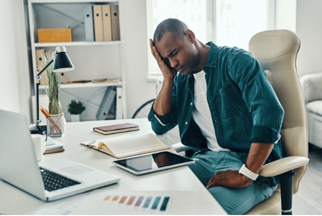 Algie vasculaire de la face : un homme à son bureau en train de se tenir un côté de la tête visiblement accablé par la douleur.