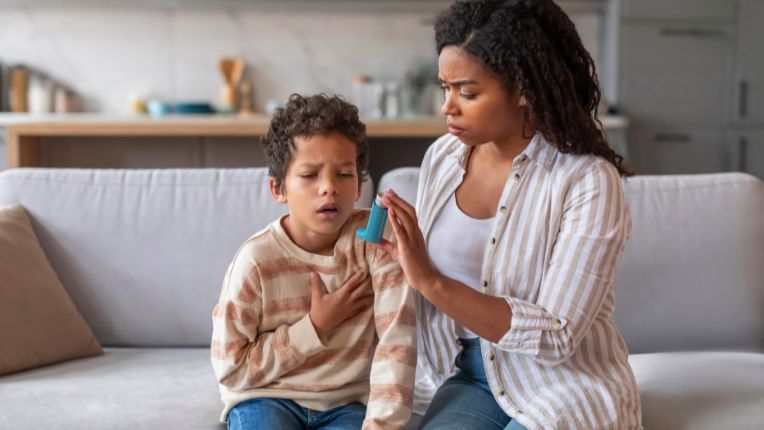 un petit garçon en plein crise avec sa main à ses côté tenant un inhalateur à la main 