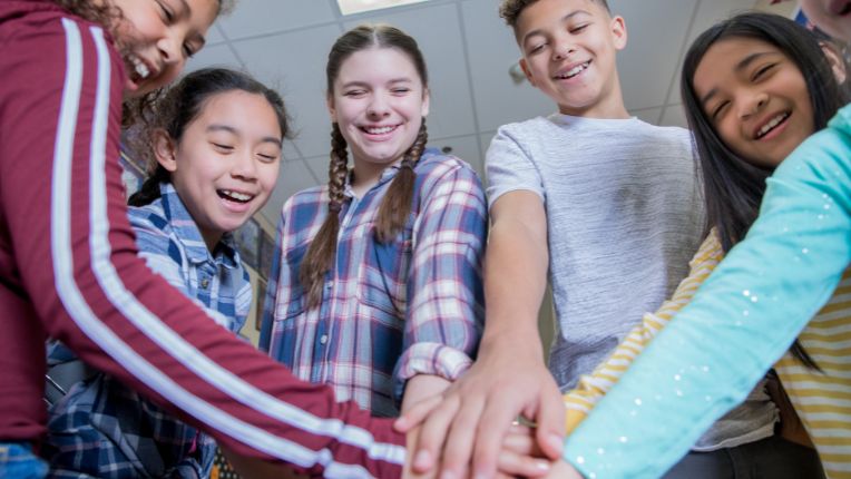 Vaccination contre le papillomavirus au collège : de jeunes collégiens joignent leurs mains en souriant.