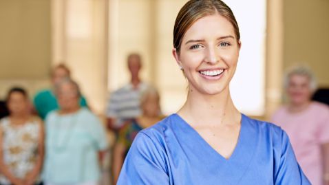 Photo d'une aide soignante souriante avec en arrière plan des patients.