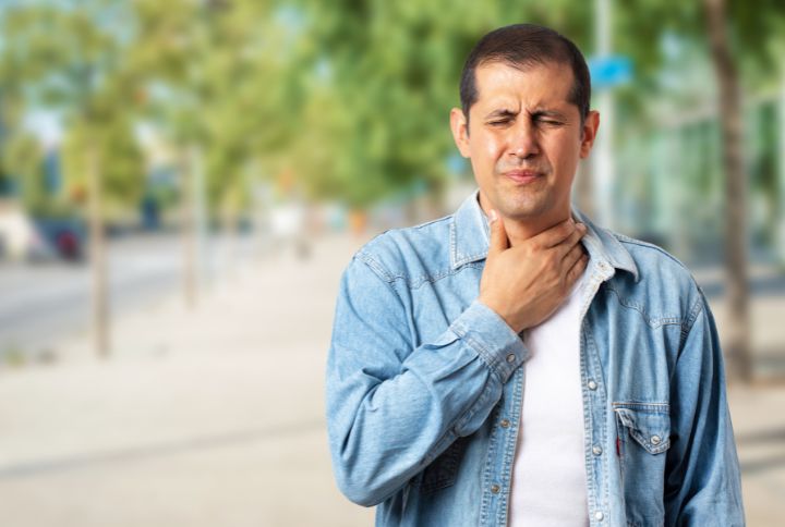 Cancer du nasopharynx : definition, symptôme, espérance de vie. Un homme met sa main à son cou dans la rue, en grimaçant..