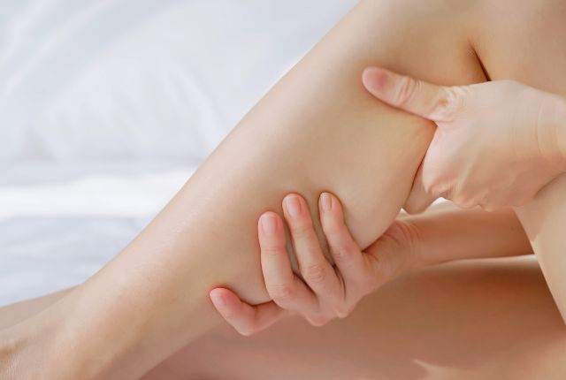 Crampes nocturnes : une femme se masse le mollet sur son lit.