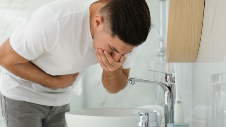 Intoxication alimentaire. Un jeune-homme pris de nausée penché au-dessus d'un lavabo.