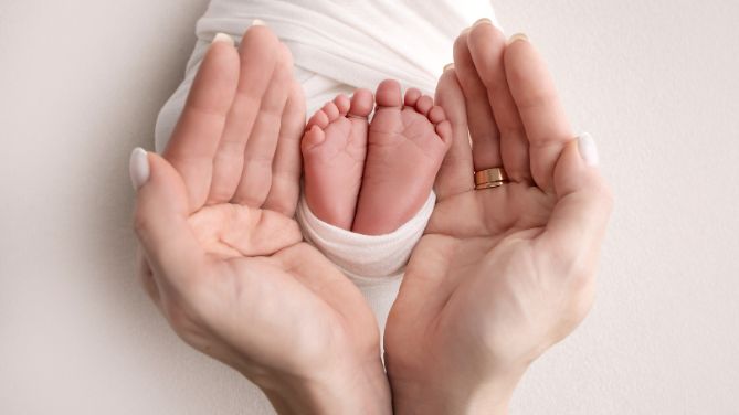 Journéé internationale de la sage femme 2025. Visuel montrant des mains de femme entourant de petits pieds de nouveau-né.
