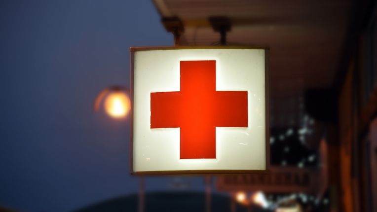 Méningites bactériennes à méningocoques. Image d'une enseigne lumineuse portant une croix rouge, marquant l'emplacement des urgences.