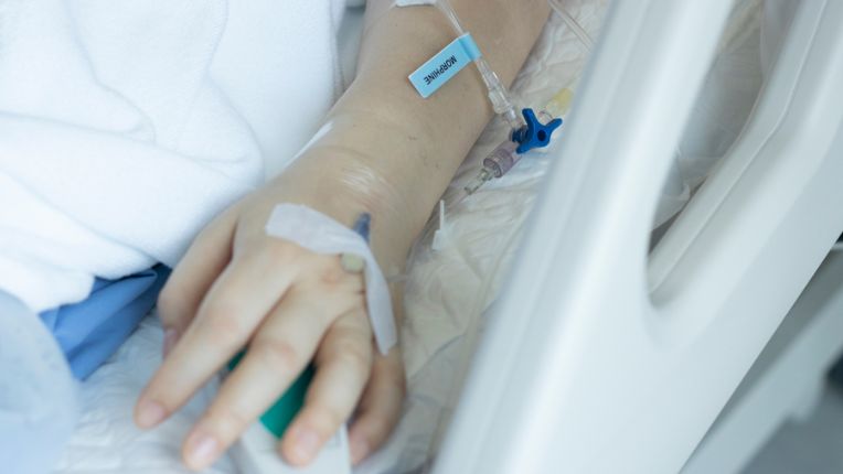 Morphine : effet secondaire, dosage, dépendance, conseil d'usage. Image montrant la main d'une patiente alitée sur lequel est fixée une canule par laquelle on lui injecte de la morphine.