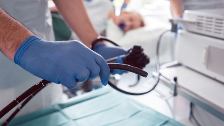 Opération de l'estomac par robot à Toulouse. Mains d'un médecin tenant des tubes au cours d'un examen de l'estomac. En arrière plan, un patient couché sur le côté.