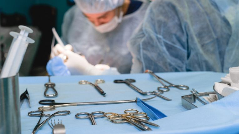Opération du rectum par robot à Valenciennes. Image d'un plateau avec des instruments chirurgicaux avec en deuxième plan des chirurgiens en pleine opération.