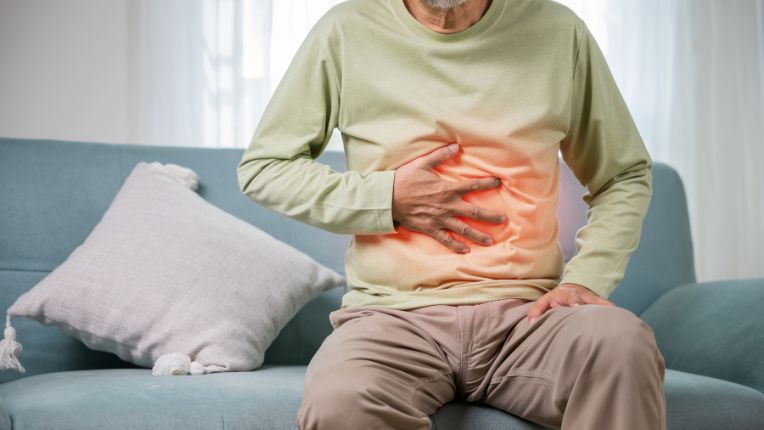 Phloroglucinol (Spasfon) : c’est quoi ? Indication, posologie (80 mg ou 160 mg). Un homme d'âge mur, assis sur un canapé, et se tenant le ventre de douleur. La douleur est figurée par un halo rouge sur son ventre.