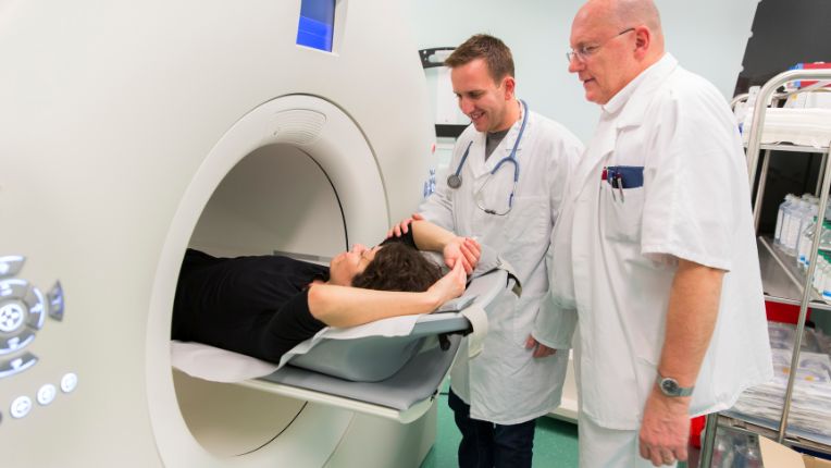 Pourquoi on fait un PET scan ? Deux soignants préparent une patiente à rentrer dans un PET scan.