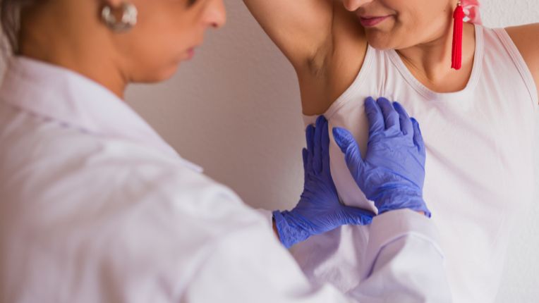 Cancer du sein. Une soignante avec des gants bleus palpe le sein gauche d'une patiente.