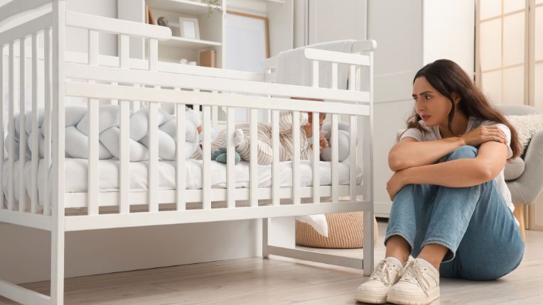Dépression post-portum. Une jeune maman anxieuse regarde son bébé derrière les barreaux de son lit.