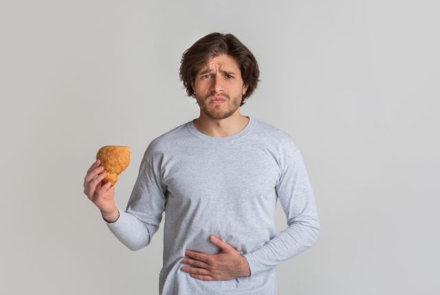 Syndrome de l'intestin irritable : un homme grimaçant tient une viennoiserie d'une main et se tient le ventre de l'autre.