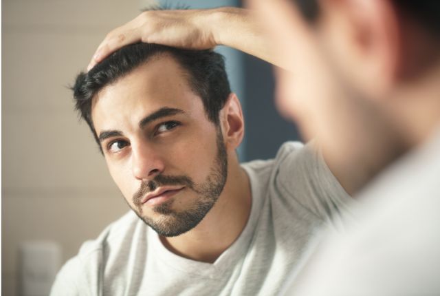 Alopécie ou perte de cheveux : un homme se scrute dans le miroir.