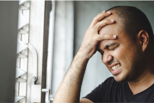 Céphalée ou mal de tête : un homme, grimaçant de douleur, se prend la tête dans la main.