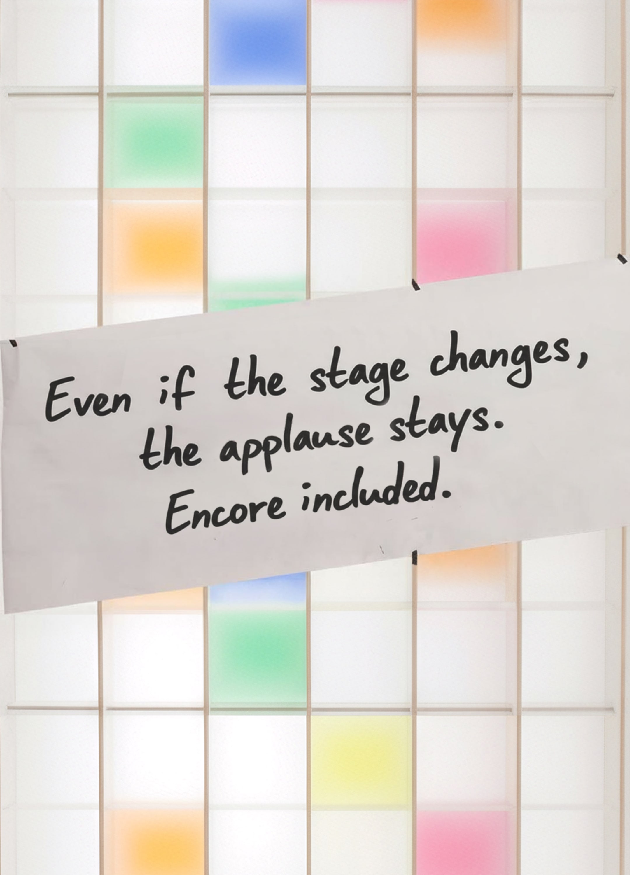 A white shelf with colorful compartments. A piece of paper with a saying hangs on the shelf: Even if the stage changes, the applause stays. Encore included.