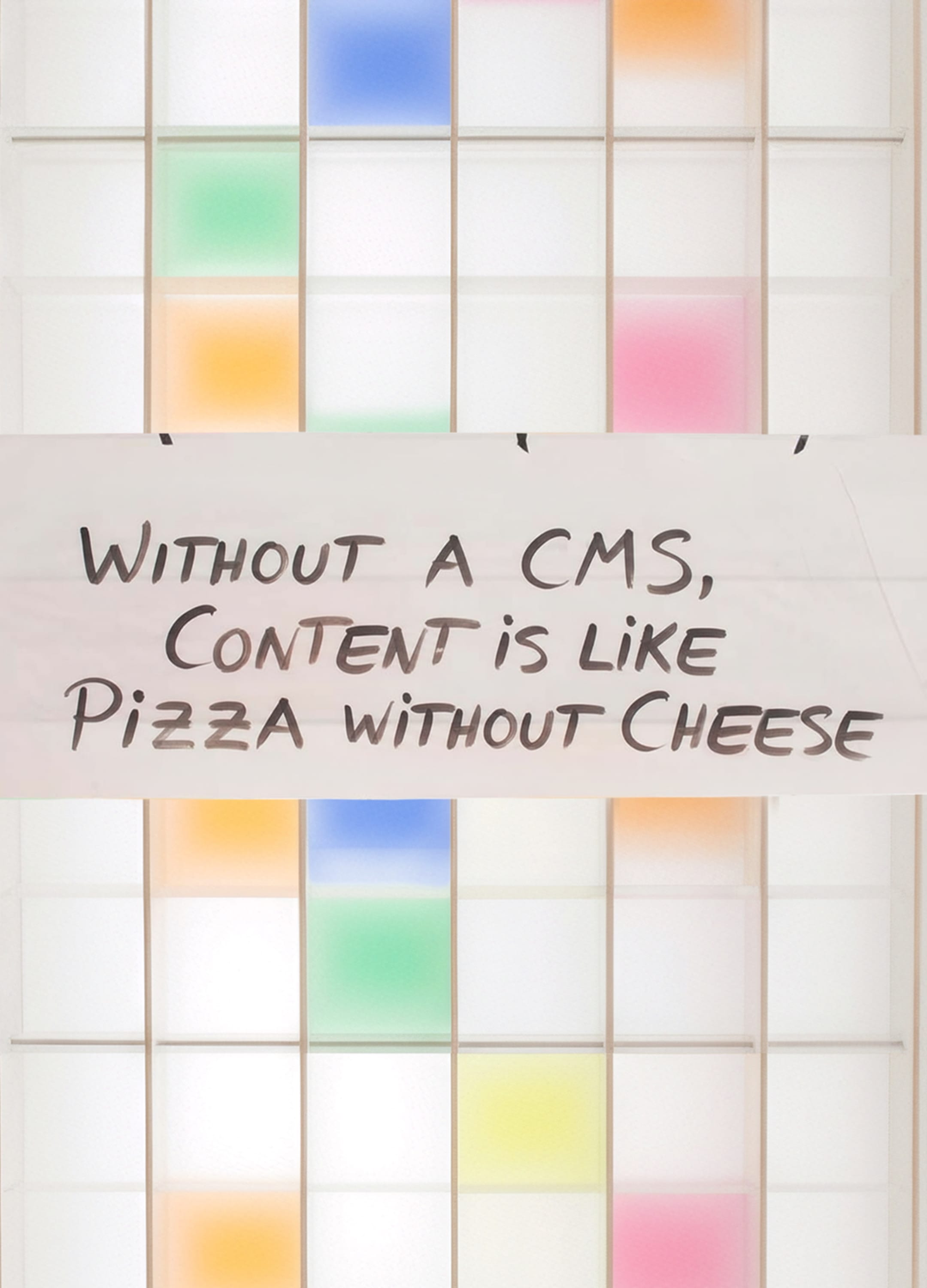 A white shelf with colorful compartments. A piece of paper hangs on the shelf with a saying: Without CMS, content is like pizza without cheese.