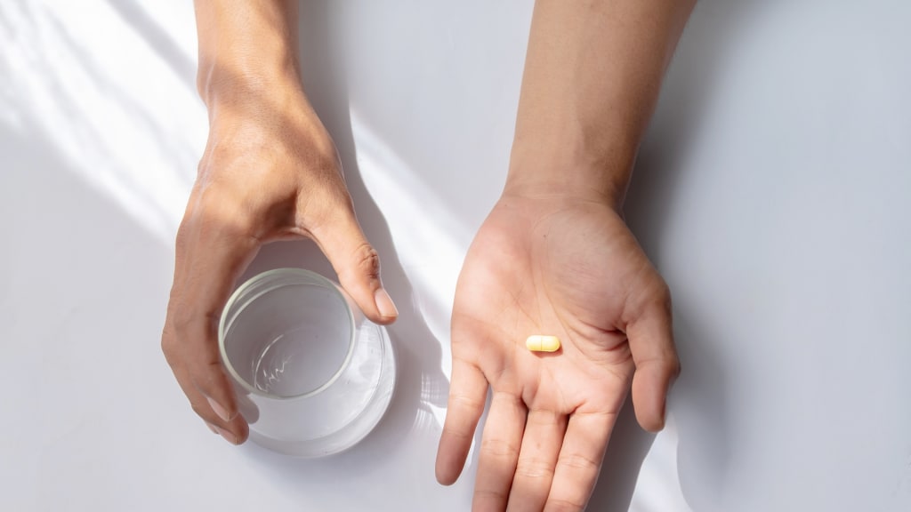 Asian man holding pills and a glass of water against a white background.