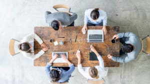 Business professionals in suits collaborate around a desk with laptops, discussing future business strategy.