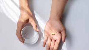 Hand mit Pillen und einem Glas Wasser