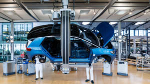 A blue vehicle without wheels or doors is being assembled in the production hall