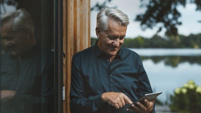 Grandpa smiles at his tablet and is standing outside in front of a wooden door