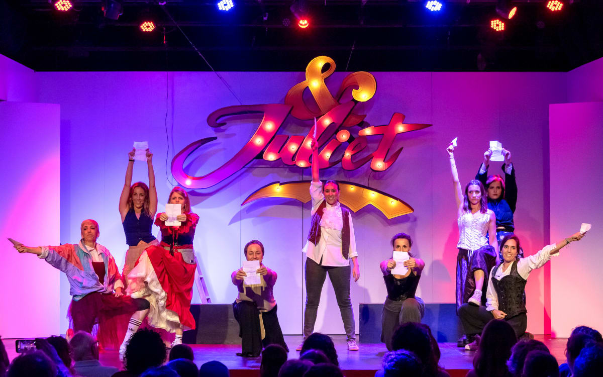 Escena de & Juliet: el elenco con hojas en la mano ante el rótulo luminoso del título
