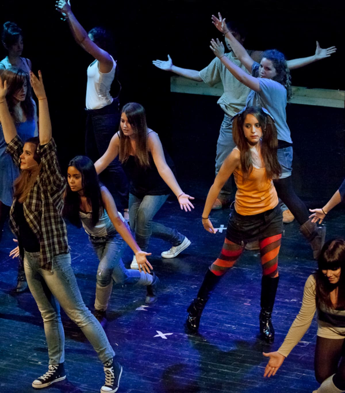 Grup nombrós ballant amb roba de carrer sota una llum blava a l'escenari