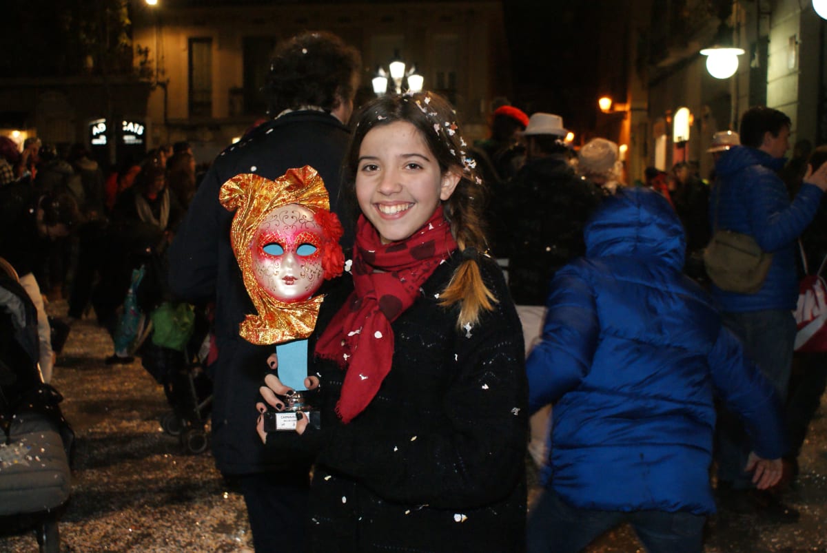 Una alumna sonríe en la calle de noche con un trofeo en forma de máscara dorada