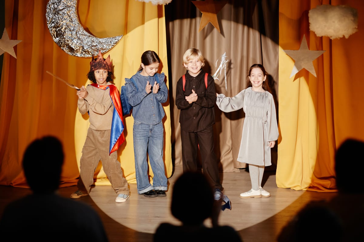 Quatre infants en escena amb decorat de lluna i estrelles, davant les siluetes del públic