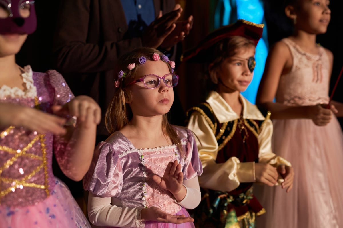 Infants amb vestits de princesa i pirata aplaudeixen a l'escenari sota llum càlida