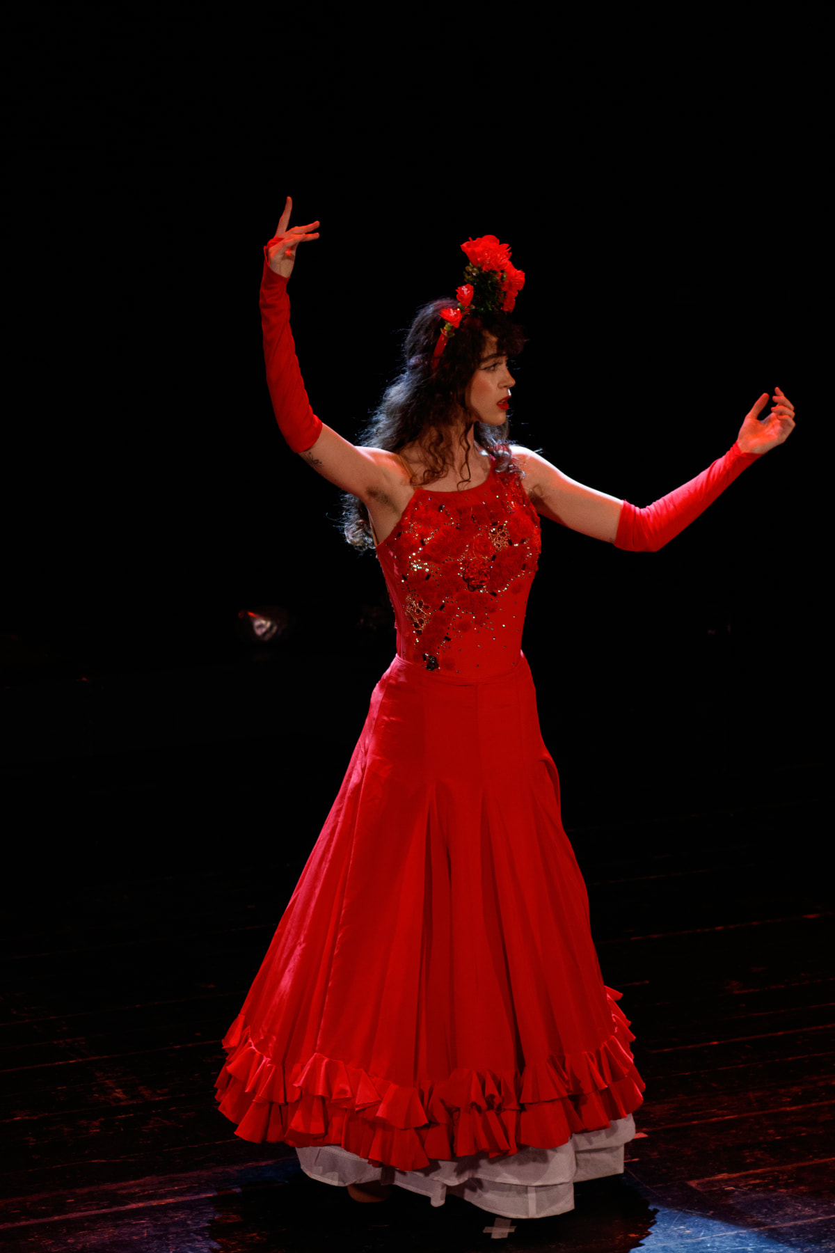 Intérprete con vestido rojo de volantes y brazos en alto sobre el escenario oscuro