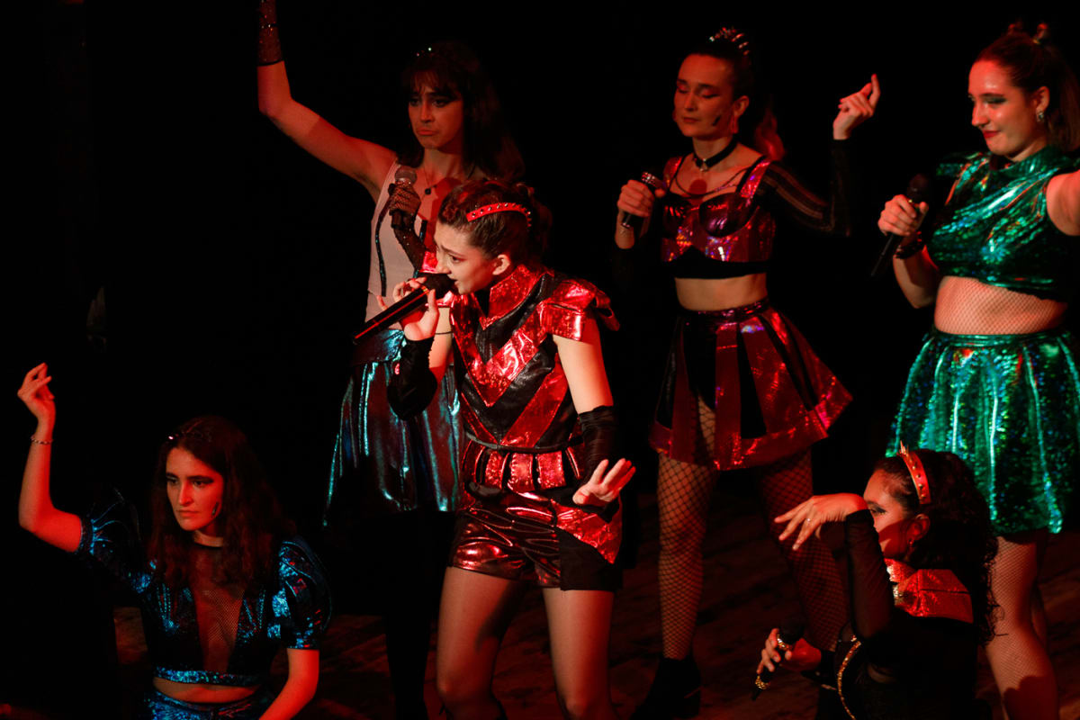 Escena de Six: seis intérpretes con trajes metalizados y micrófonos bajo luz roja