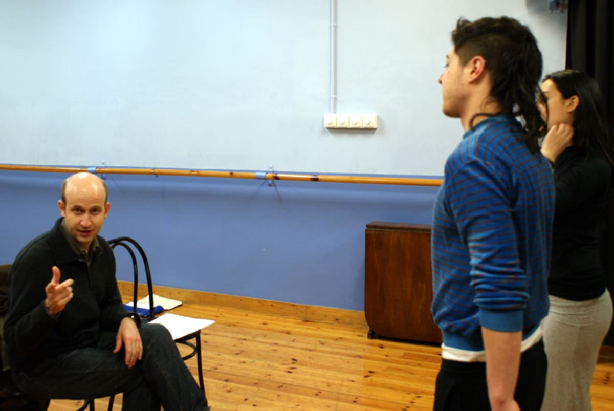 Un profesor sentado da indicaciones a dos alumnos en un aula con barra de danza