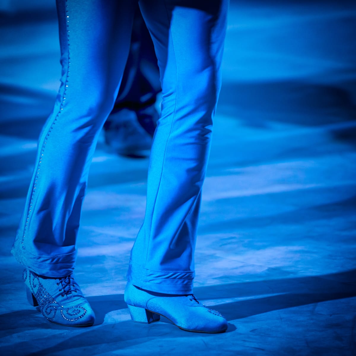 Detalle de piernas y zapatos de baile bajo una luz azul intensa