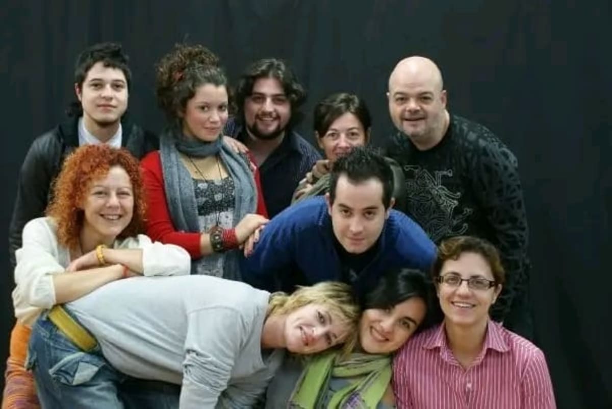Foto de grupo de una compañía: diez intérpretes sonríen apiñados ante un fondo negro