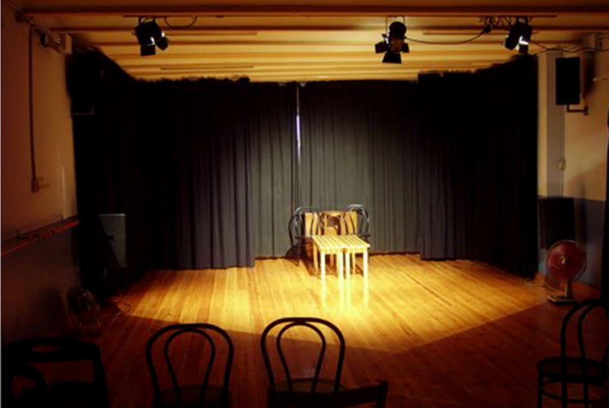 Escenario de la sala iluminado con focos, con una mesa y sillas en el centro