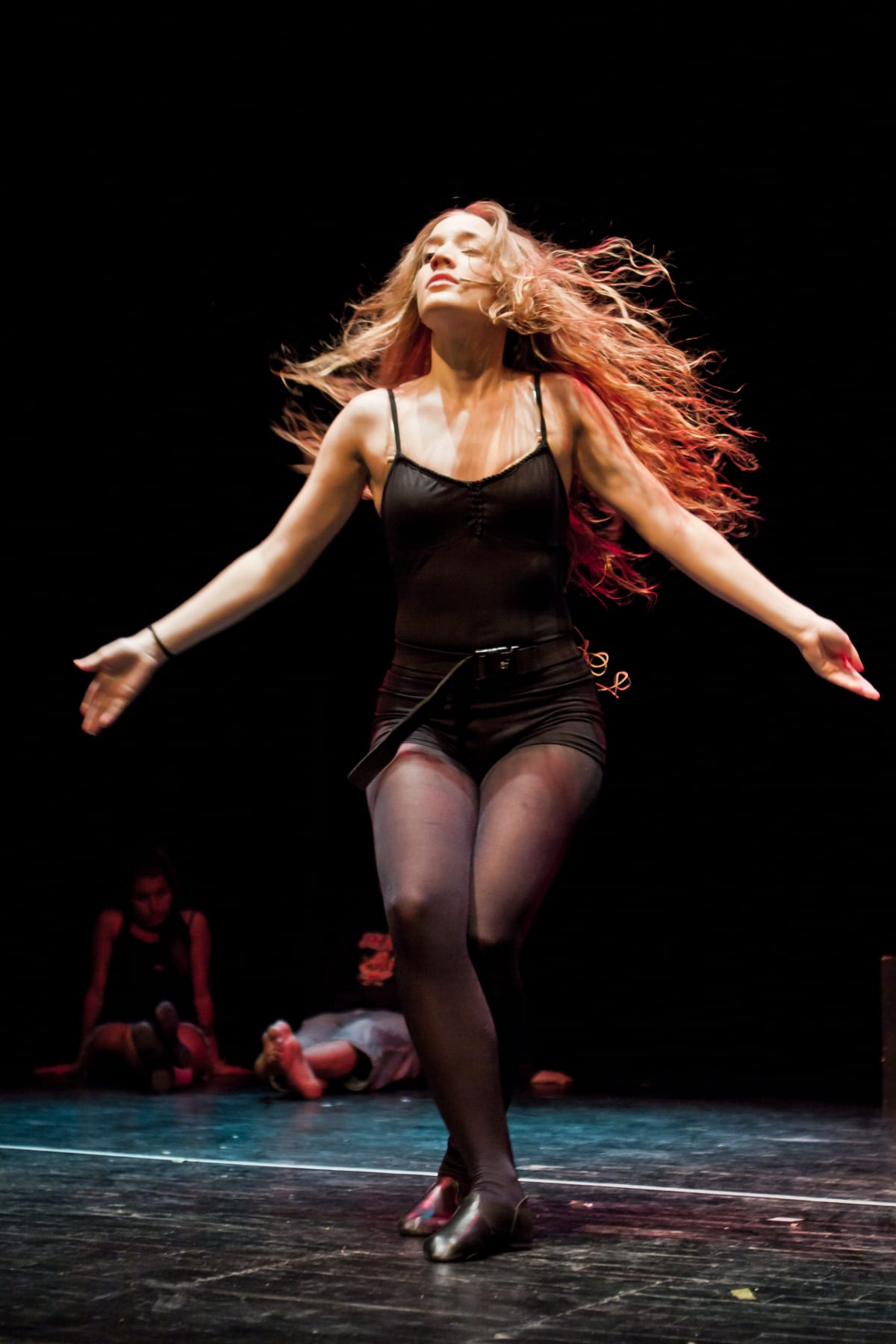 Ballarina amb els cabells al vent i els braços oberts al centre de l'escenari