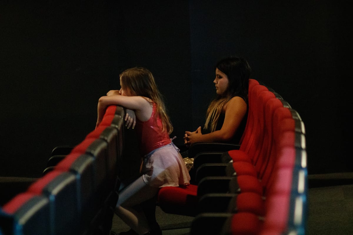 Dos alumnas charlan sentadas en las butacas rojas de la sala a oscuras