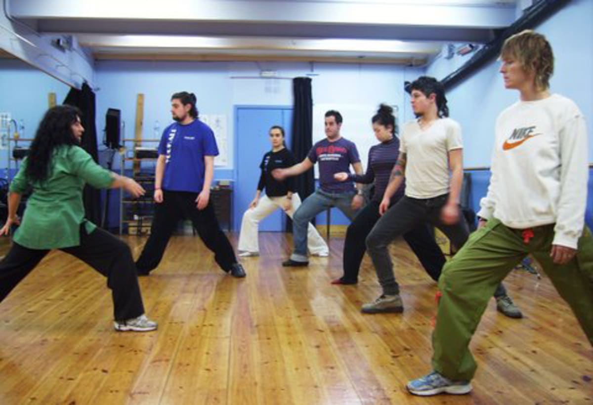 Alumnos adultos hacen un ejercicio de movimiento en un aula de parquet y paredes azules