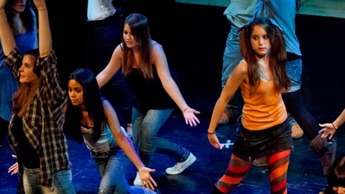 Detall d'una coreografia de grup amb roba de carrer sota llum blava